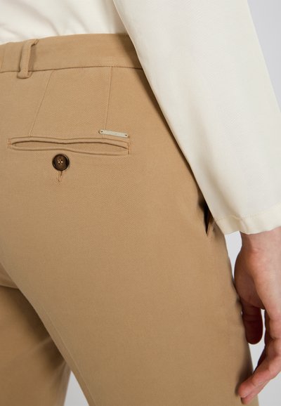 Beżowe spodnie z teksturowanym wykończeniem, z tylną kieszenią zapiętą brązowym guzikiem oraz małą ozdobną metką.