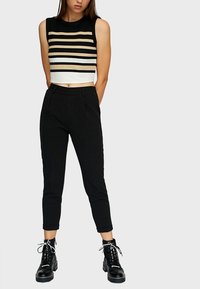 Top court sans manches noir à rayures beige et blanches, associé à un pantalon noir ajusté et des bottes à lacets chunky noires.