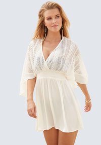 Abito bianco con scollatura a V, dettagli in pizzo elaborati sulla parte superiore e maniche fluide. Tessuto morbido e leggero con una vestibilità comoda.