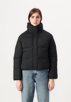 Black cropped puffer jacket with a high collar, featuring quilted sections, soft texture, and front zip closure. Paired with light blue jeans.