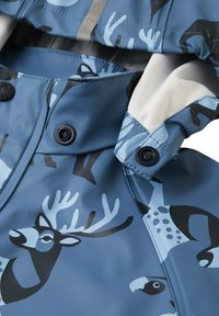 Giacca impermeabile blu con motivi animali neri e azzurri. Presenta chiusure a scatto e una texture liscia e lucida.