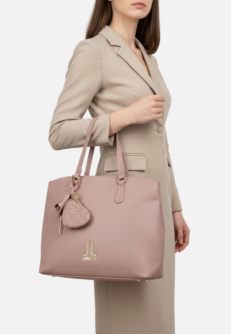 Borsa sintetica rosa soffice con dettagli in oro, superficie testurizzata, doppio manico e un piccolo portachiavi a forma di cuore attaccato.