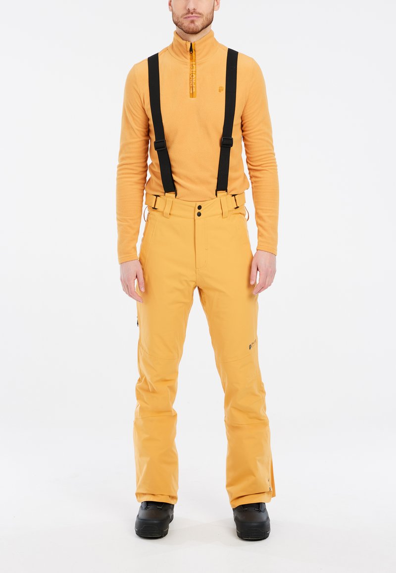 Completo da sci maschile con un top in fleece arancione con zip a un quarto e pantaloni impermeabili gialli con bretelle nere e tasche.