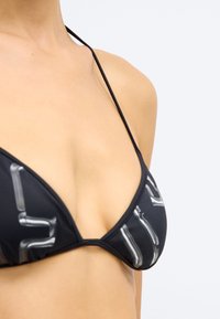Μαύρο μπικίνι τοπ με τριγωνικές θήκες, λεπτές τιράντες και λευκό γεωμετρικό μοτίβο. Λείος υφή με εφαρμοστή σχεδίαση.