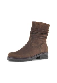 Bottine en suede marron mi-mollet avec un dessus relâché, bout rond, couture visible, et une semelle en caoutchouc noir basse avec des crampons.