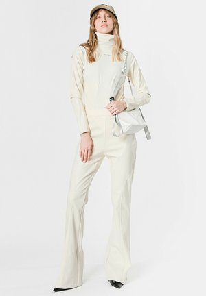 Mono color crema con cuello alto, mangas largas y pantalones acampanados. Combinado con un bolso gris cruzado y una gorra clara.