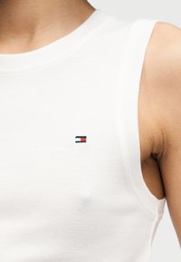 Λευκό βαμβακερό αμάνικο τοπ με ένα μικρό κεντημένο λογότυπο σε ναυτικό μπλε και κόκκινο. Το ύφασμα έχει λεία υφή με εφαρμοστή σχεδίαση.