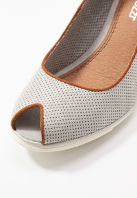 Scarpa in tessuto perforato grigio con design open-toe, accentuata da un bordo marrone e una soletta texturizzata. Suola in gomma visibile sulla punta.