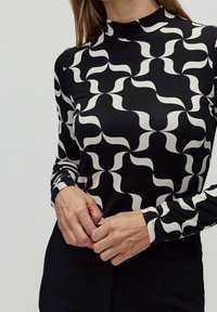 Svart och vit mönstrad långärmad topp med hög krage, som har vågiga abstrakta former och en slät, figurnära textur.