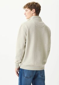 Light grey pullover sweatshirt, soft fabric, high collar, relaxed fit, ribbed cuffs and hem, paired with blue jeans, viewed from the back.