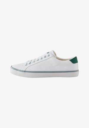 Niski biały sneaker z białymi sznurowadłami, szarą lamówką podeszwy i zielonym paskiem na pięcie na czystym białym tle.