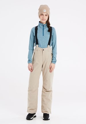Completo invernale a due pezzi composto da una maglia a maniche lunghe blu con zip e pantaloni impermeabili beige con bretelle nere regolabili e zip.