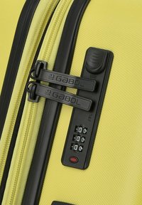 Valigia gialla con una superficie testurizzata, dotata di due cerniere nere e di un lucchetto a combinazione con un pulsante di reset rosso.