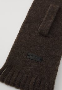 Gant en laine brun avec une petite étiquette noire portant "PURE PURE" et une sangle autour du poignet, sur fond blanc.