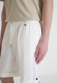 Shorts bianchi realizzati in un tessuto leggero, con vita elasticizzata e cordoncino. Accenti con bottoni all'orlo e tasche laterali.