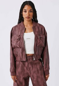 Bomberjack in bordeaux nepleer, verkorte ontwerp met twee voorzakken, ribgebreide boorden en zoom, gecombineerd met bijpassende cargobroek.