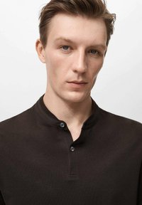 Cămașă henley neagră cu guler mic, având două nasturi la gât. Textură de țesătură netedă și croială ajustată.