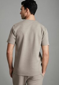 Tricou gri, cu mânecă scurtă, realizat dintr-un material moale și texturat, având decolteu tip crew și o croială lejeră.