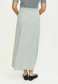 Sivá, po kolená dlhá, ľahká džersejová sukňa s elastickým pásom, hladkou textúrou a rovnou siluetou. Nosená s čiernymi balerínkami.