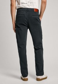 Tumed hallid chinosid kitsas lõikes, lukustatavad tagataskud ja pruun nahast silt vööl. Kannab valgeid tossusid.