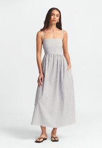 Abito maxi a righe con corpetto aderente e gonna svasata. Realizzato in tessuto leggero con spalline sottili e tasche laterali.