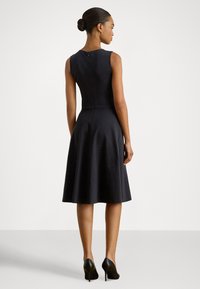 Piedurkņu melna kleita līdz ceļiem ar pieguļošu augšdaļu un izplatītu svārku. Aizmugurē rāvējslēdzēja aizdare, gluda tekstūra un minimāls dizaina izpildījums.