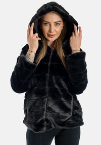 Giacca felpa nera in pelliccia sintetica con chiusura a zip, caratterizzata da un motivo testurizzato e un cappuccio. Materiale morbido e peloso con vestibilità comoda.