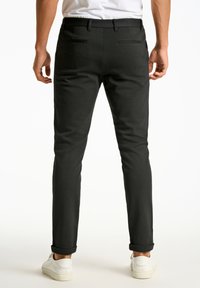 Sorte slim-fit bukser med en glat tekstur, to baglommer og opbukket kant, kombineret med hvide sneakers.