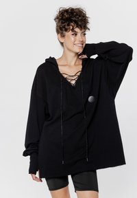 Czarna, oversize bluza z kapturem z wiązaniem przy dekolcie i metalowymi sznurkami; wykonana z miękkiego materiału o luźnym fasonie i ściągaczami przy nadgarstkach.