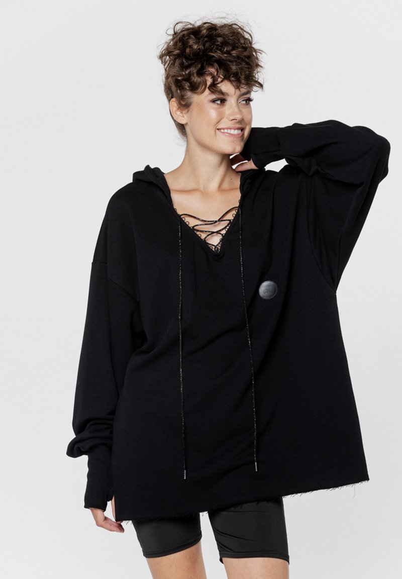 Czarna, oversize bluza z kapturem z wiązaniem przy dekolcie i metalowymi sznurkami; wykonana z miękkiego materiału o luźnym fasonie i ściągaczami przy nadgarstkach.