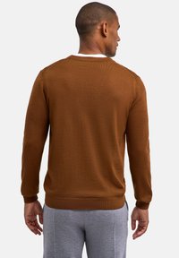 Maglione di lana marrone con scollatura rotonda e polsini a coste. Indossato con pantaloni felpati grigi, che mostrano una texture liscia e un design aderente.