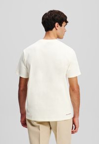 Crème-kleurig katoenen t-shirt met korte mouwen en een ronde hals, met een klein logo aan de onderrand aan de linkerkant.