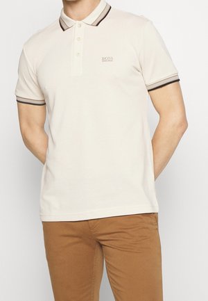Beige poloshirt lavet af bomuld med krave, tre-knaps åbning og kontrasterende mørke stribede detaljer på krave og ærmer.