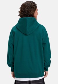 Sudadera de algodón en color verde azulado, con una gran capucha, puños y dobladillo acanalados, que presenta un corte holgado y una vista trasera. Textura suave, sin patrones visibles.
