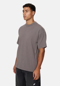 Grijze katoenen t-shirt met een relaxte pasvorm, ronde hals en contrasterende stiksels langs de zijkanten. Tentoongesteld op een neutrale achtergrond.