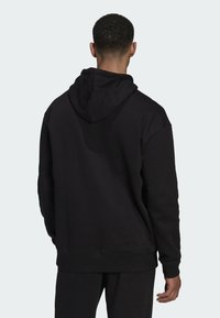 Sudadera negra con capucha que presenta un acabado texturizado, puños acanalados y un ajuste relajado. Costuras visibles en las costuras y una capucha amplia.