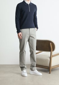 Navy zippered sweater, light gray chinos, and white sneakers. The sweater has a collar; pants feature a tailored fit and smooth texture.