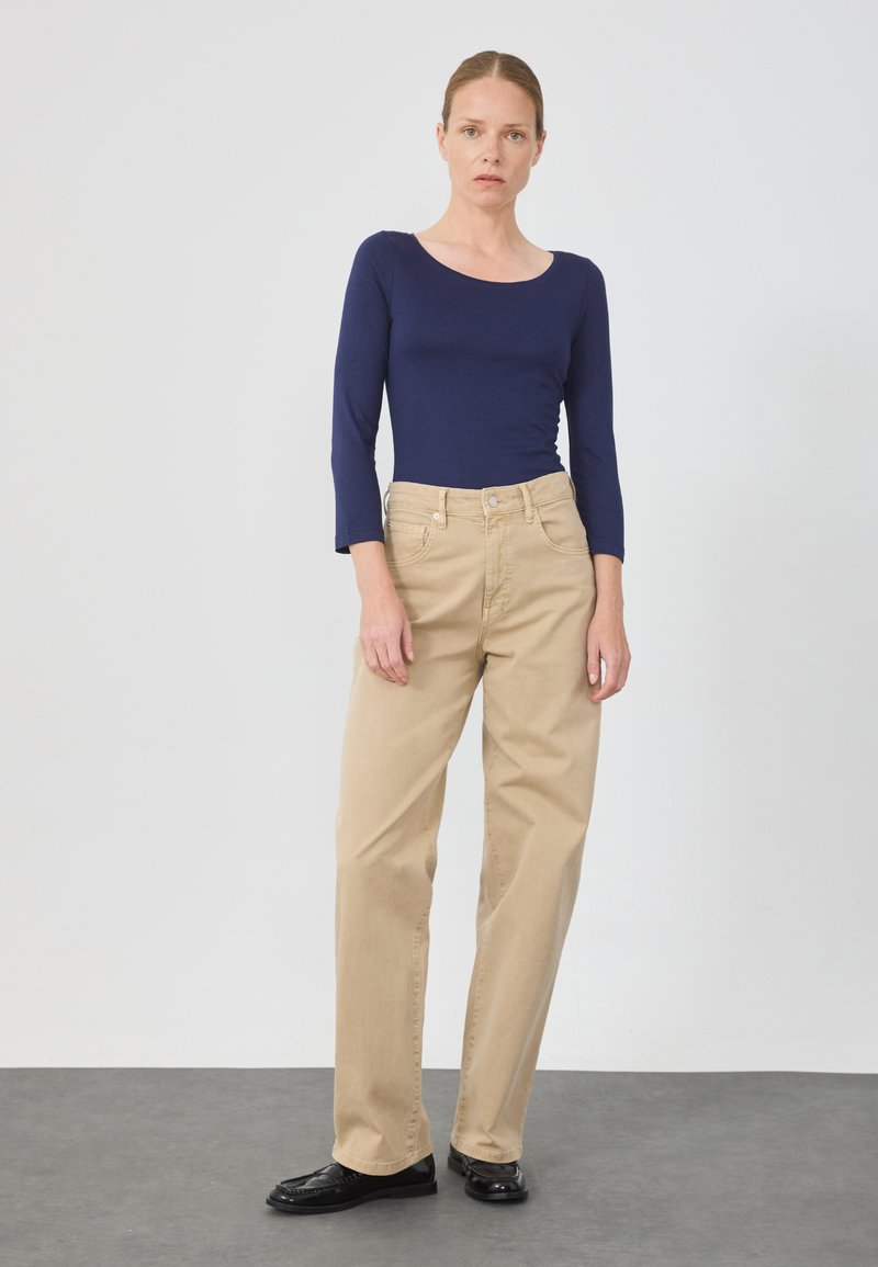 Top fitted a maniche lunghe blu navy abbinato a pantaloni beige chiaro a gamba dritta e mocassini neri. Texture dei tessuti liscia e elementi di design classici.