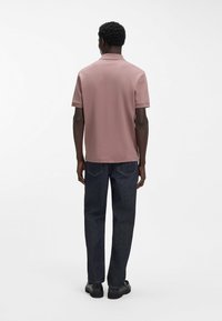 Polo rosa chiaro con colletto e maniche corte, abbinata a jeans blu scuro a gamba dritta e scarpe nere. Tessuto liscio e vestibilità classica.