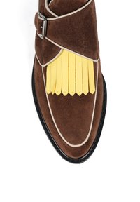 Brązowy zamszowy but z żółtymi skórzanymi frędzlami, białą lamówką wzdłuż krawędzi i srebrnym zapięciem na pasku.