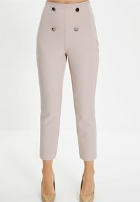 Hoge taille, taps toelopende broek van zacht beige stof met twee zwarte knopen als detail, met een gladde textuur en een op maat gemaakt silhouet.