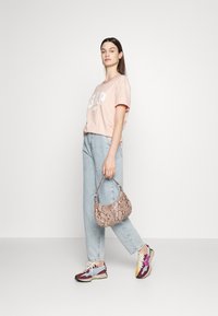 T-shirt rosa claro com o logótipo "GAP", jeans de denim desbotados e relaxados, bolsa de mão com padrão de pele de cobra e ténis coloridos com formas variadas.