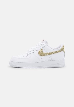 Biały niskoprofilowy sneaker z beżowym wzorem paisley na znaku i języku, białymi sznurowadłami i grubą podeszwą na jednolitym tle.