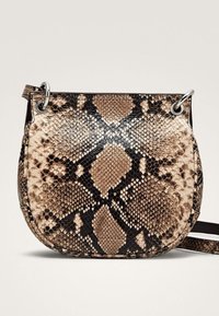 Snydebælte-crossbody taske i tan og sort, med rund form, glat tekstur, sølv hardware og en enkelt justerbar rem.