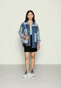 Τζιν oversized πουκάμισο με πατσαβούρα σε μπλε και γκρι, γκρι crop top, μαύρη μίνι φούστα και λευκά αθλητικά παπούτσια με μαύρες λεπτομέρειες. Μικρή γκρίζα τσάντα.