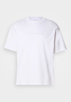 T-shirt in cotone bianco con maniche corte, con un logo Calvin Klein in rilievo al centro. Design classico con colletto girocollo. Tessuto liscio.