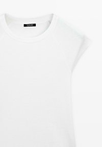 T-shirt blanc à manches courtes avec col rond, manches raglan et une étiquette noire visible à l’intérieur du col.