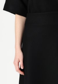 Black wool-blend dress with a loose fit and short sleeves. The fabric has a soft texture, complemented by a smooth waistband detail.