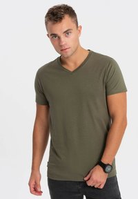 Olivengrøn kortærmet V-hals t-shirt i et glat, blødt stof. Har et tætsiddende design, båret med mørke jeans og et sort ur.