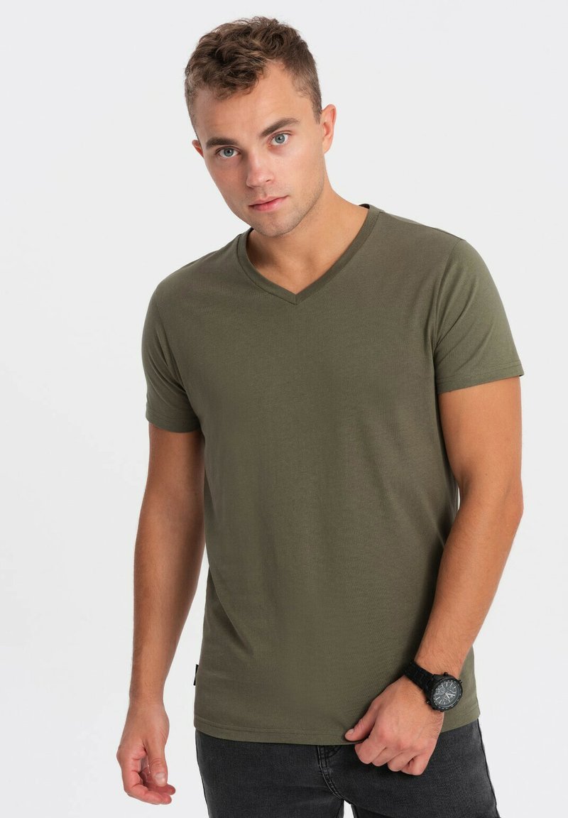 Olivengrøn kortærmet V-hals t-shirt i et glat, blødt stof. Har et tætsiddende design, båret med mørke jeans og et sort ur.